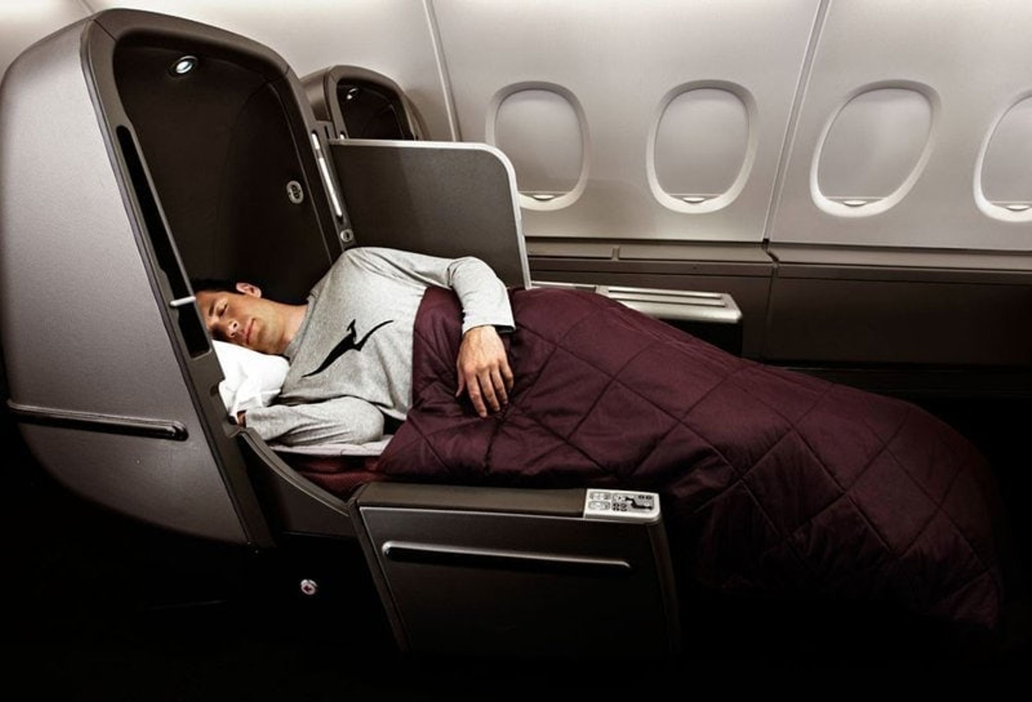 Passenger sleeping under a blanket in a Qantas business class lie-flat bed