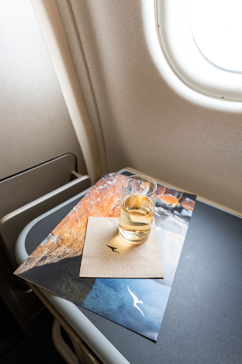 Drink and Qantas napkin on a tray table beside the window