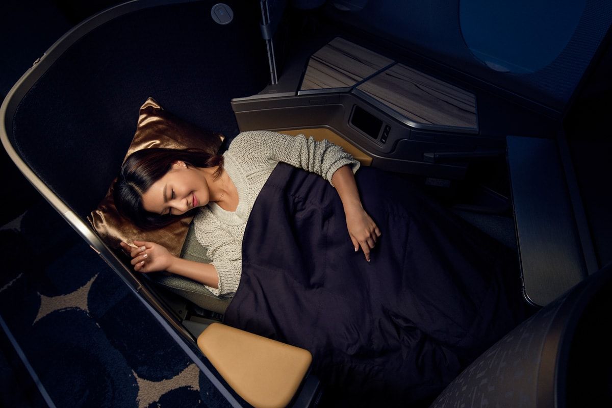 Passenger sleeping under a blanket in a lie-flat business class seat