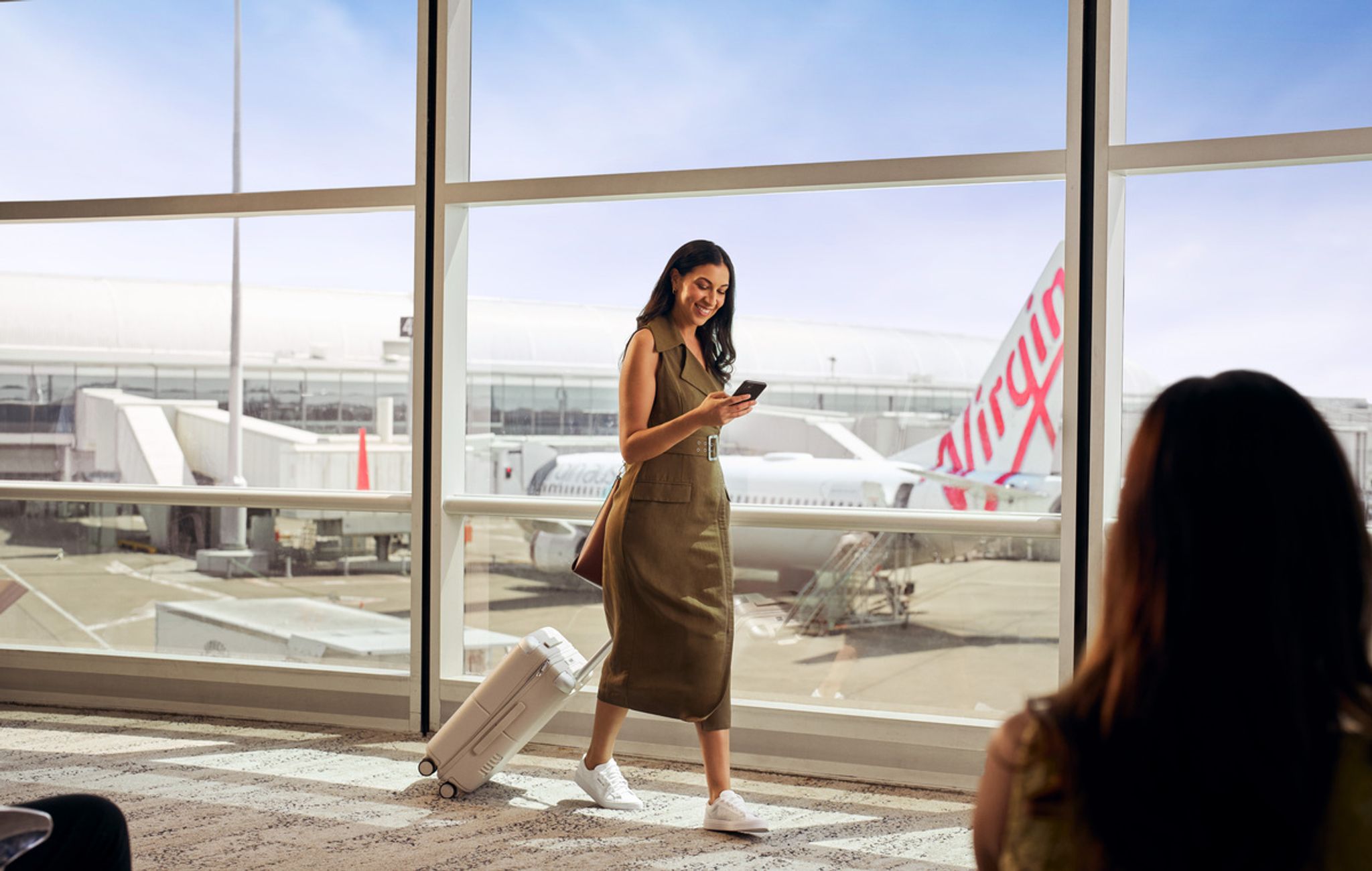 Traveller with a suitcase walking through a terminal with a Virgin Australia aircraft outside