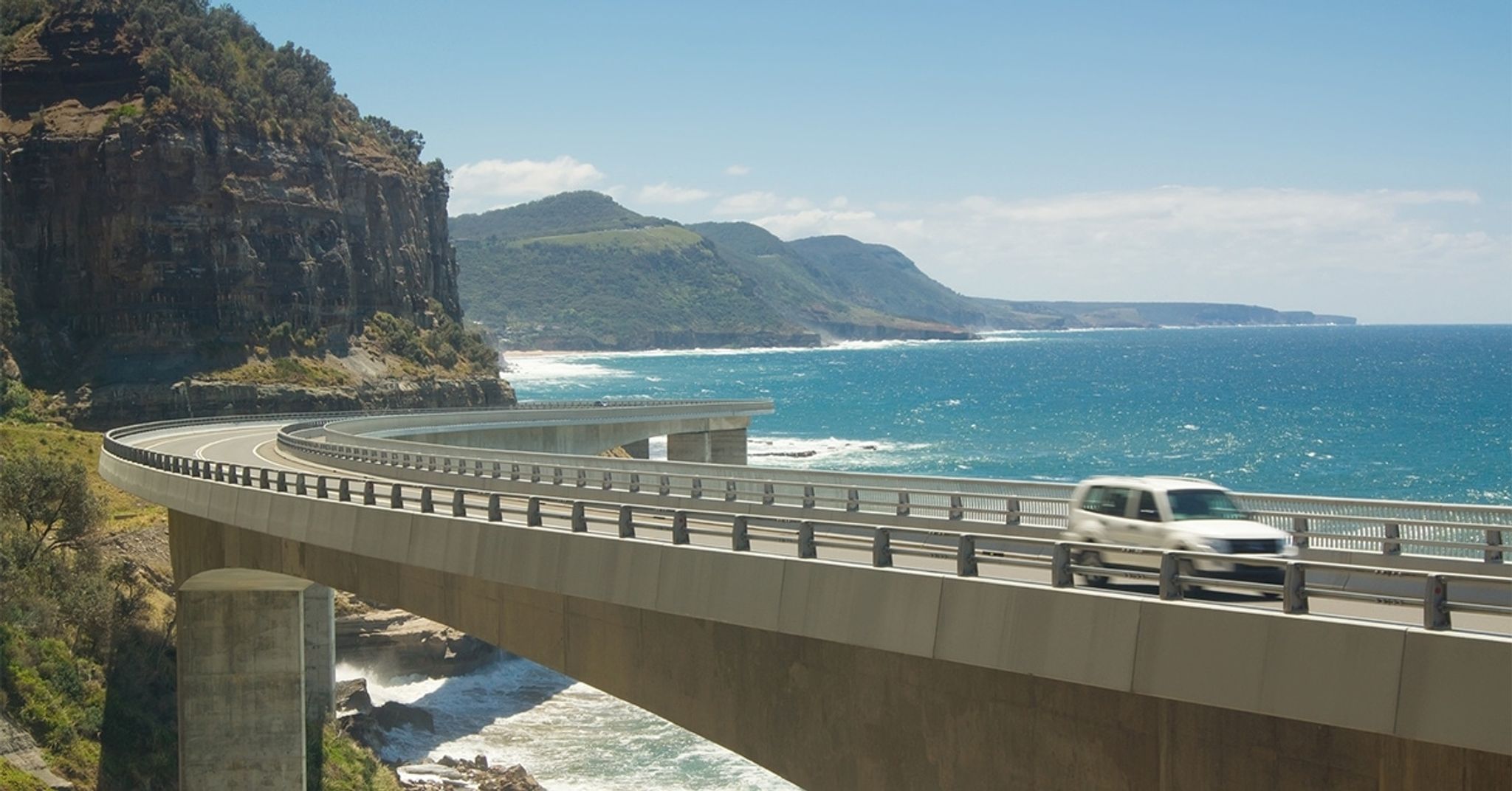 Car driving across a coastal bridge beside sea cliffs