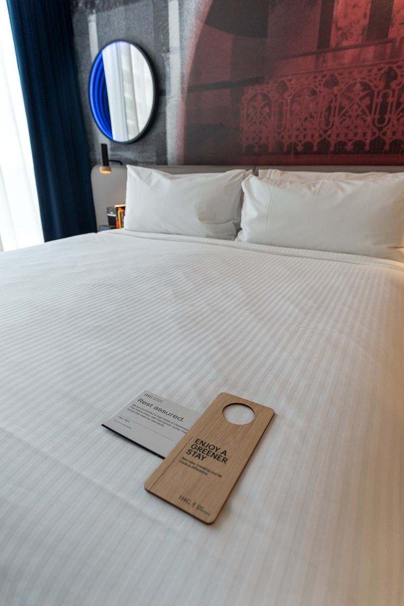 Bed made up with a green stay door hanger at Hotel Indigo Sydney