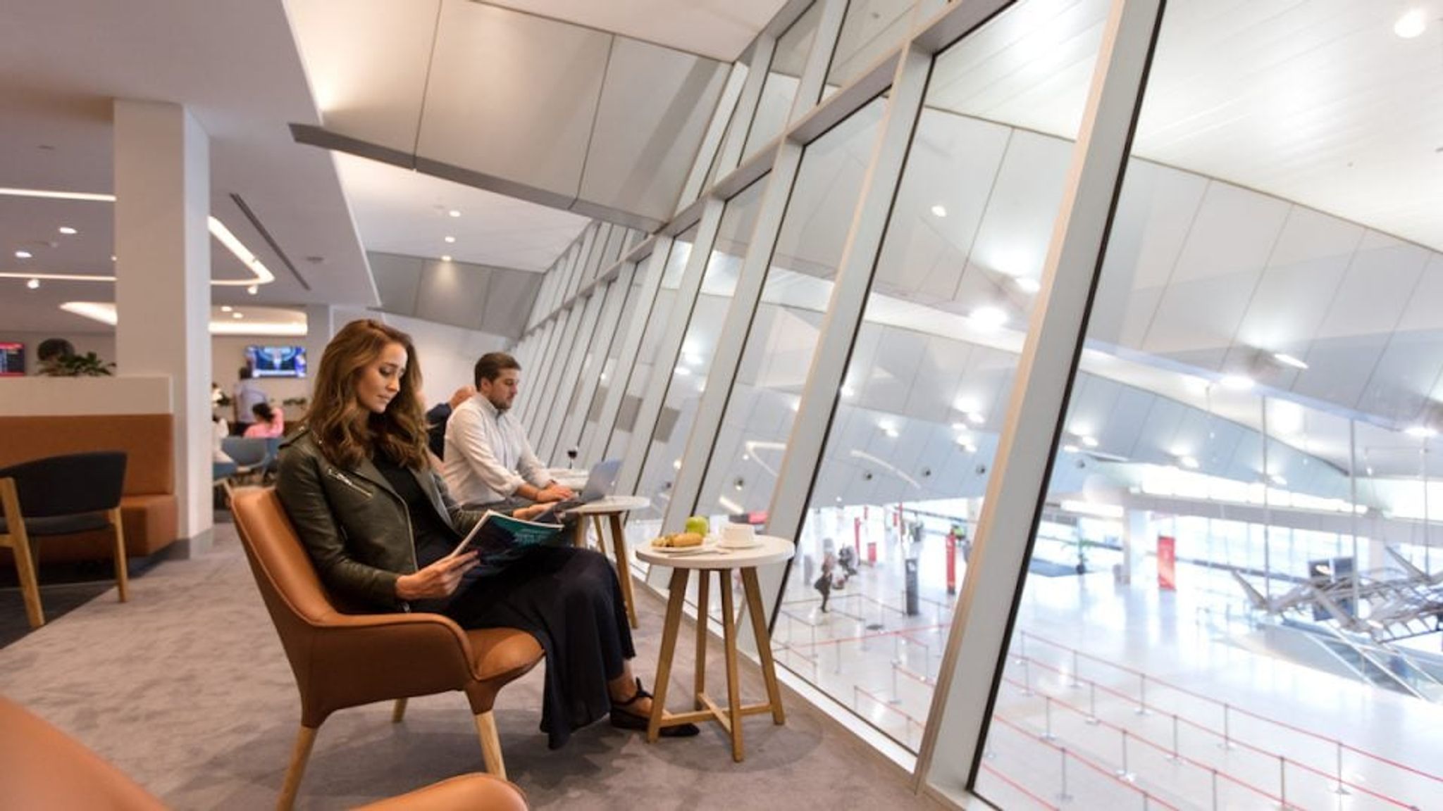 Travellers relaxing in an airport lounge beside large windows