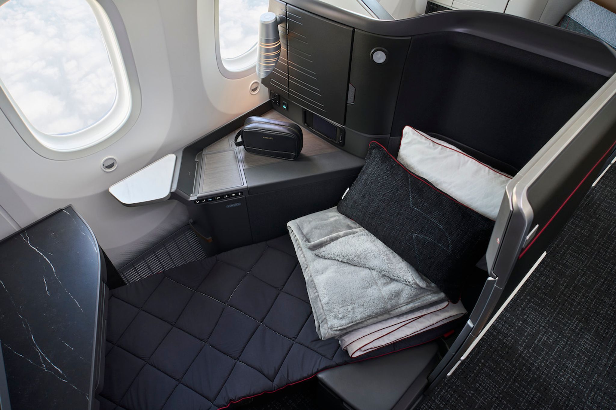 Business class seat made up with a pillow and blanket beside the window