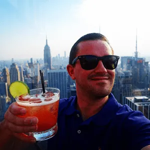 Chad S holding a cocktail on a rooftop with the New York City skyline behind